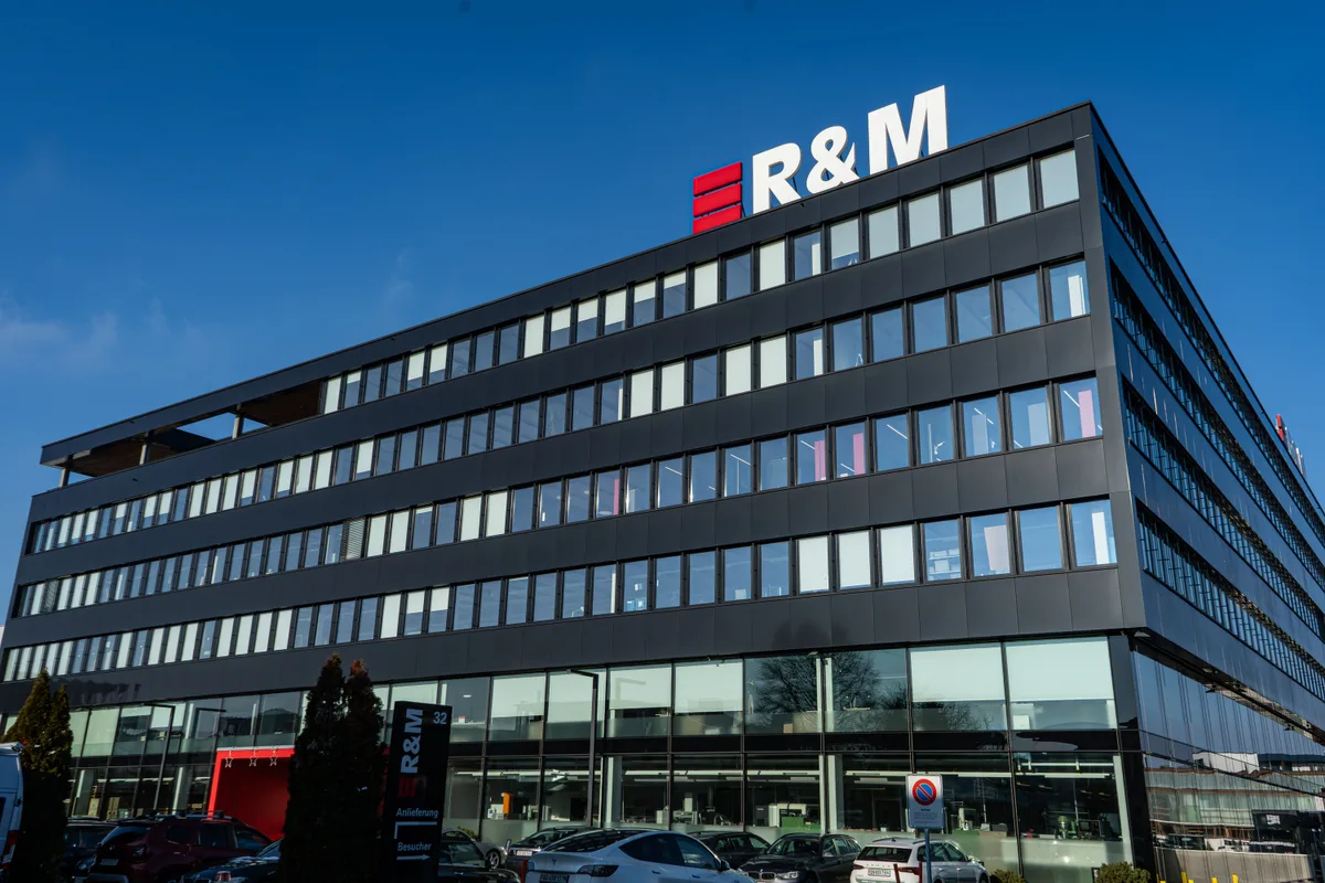Der «Kubus» in Wetzikon ist der Hauptsitz von R&M. Das Unternehmen beschäftigt weltweit rund 1700 Mitarbeitende. Der Hauptsitz von R&M in Wetzikon. Ein modernes kubisches Bürogebäude mit mehreren Stockwerken. Am Dach prangt das Logo «R&M».